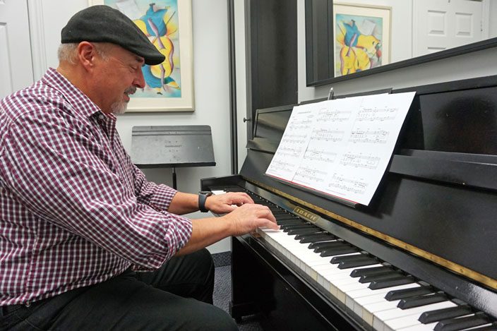 An adult male student learning to play an Ibach upright piano at a music school in Mississauga