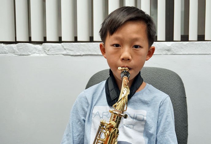 A young boy practicing playing the alto saxophone with focus, seated and holding the instrument