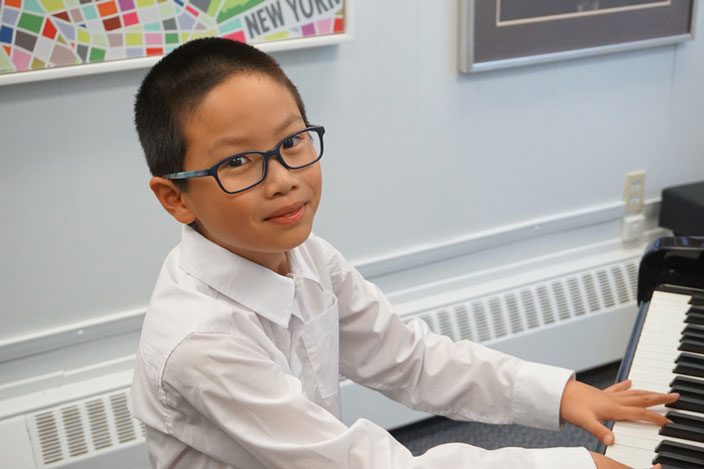 Young boy playing the keys of a grand piano during his music lesson