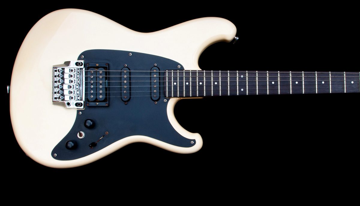Closeup of a white electric guitar body and neck against a black background
