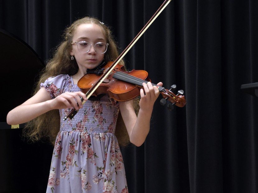 Young girl with glasses playing violin on stage