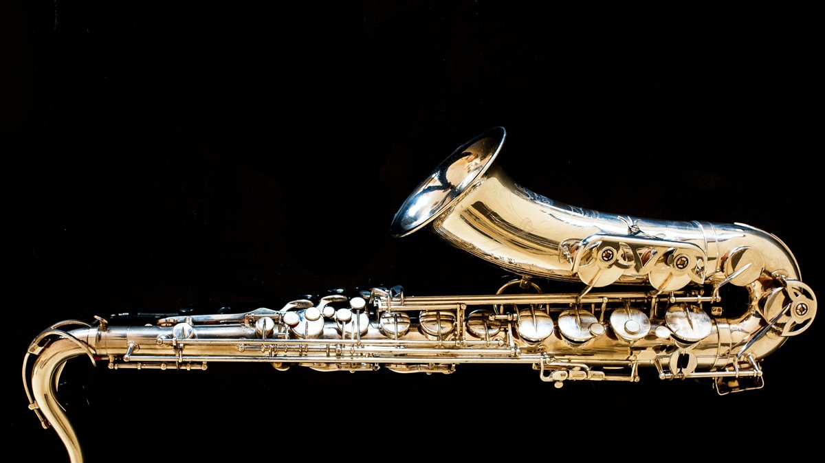 Close-up of a gold saxophone bell and keys lit against a dark background