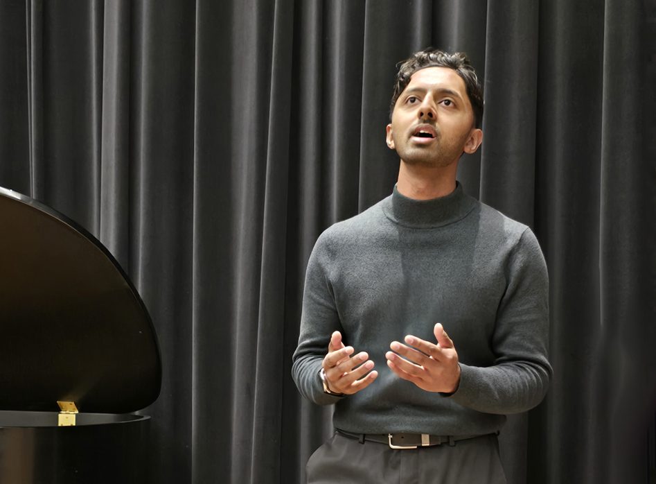 Adult male student singing in front of a dark stage curtain, preparing for an RCM voice exam