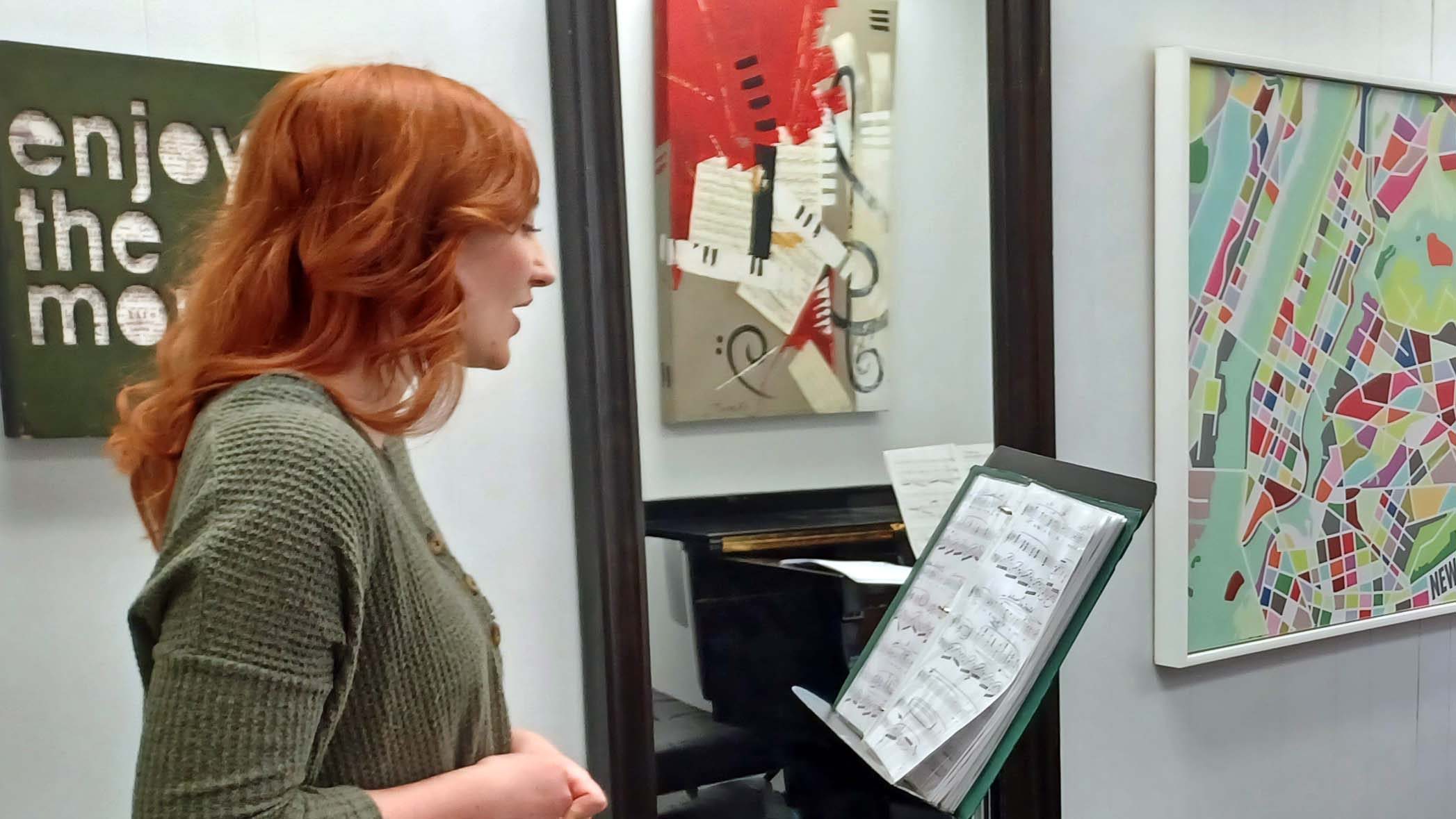 Student practising a solo with sheet music in front of a mirror during a voice lesson