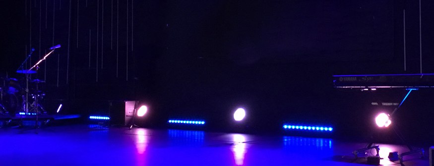 Stage with blue and pink performance lighting, drum kit and keyboard set up