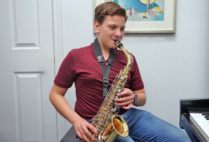 Teenage boy playing the saxophone during his music lesson with a piano in the room