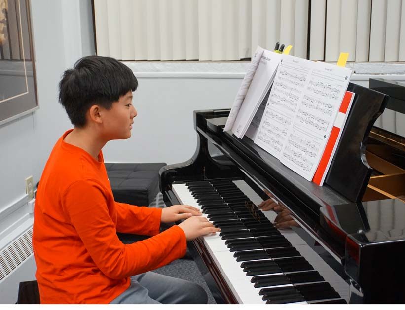 A teenage boy sitting at a Schimmel grand piano, playing advanced music