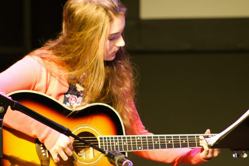 Teenage girl looking at the fretboard while playing acoustic guitar on stage