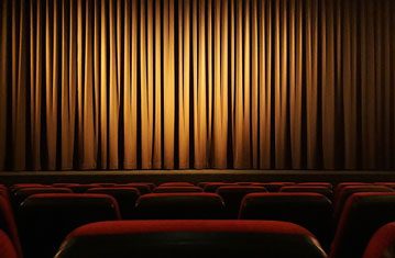 Empty theatre seats facing a lit stage curtain