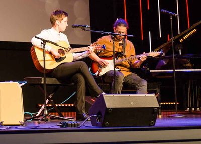 Two guitarists performing a duet together on stage at a recital