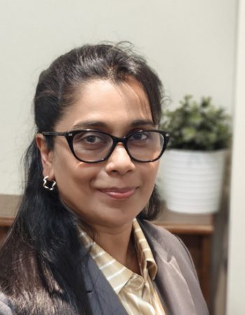 Portrait of a piano teacher in Mississauga, sitting at an upright piano and smiling.